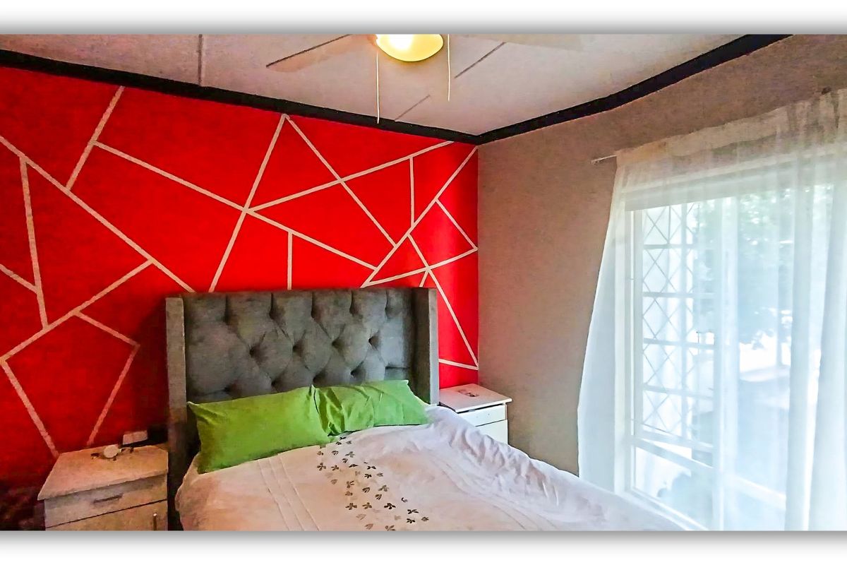 A bedroom featuring a geometric accent wall, ceiling fan, and a sliding glass door with security gate providing natural light.