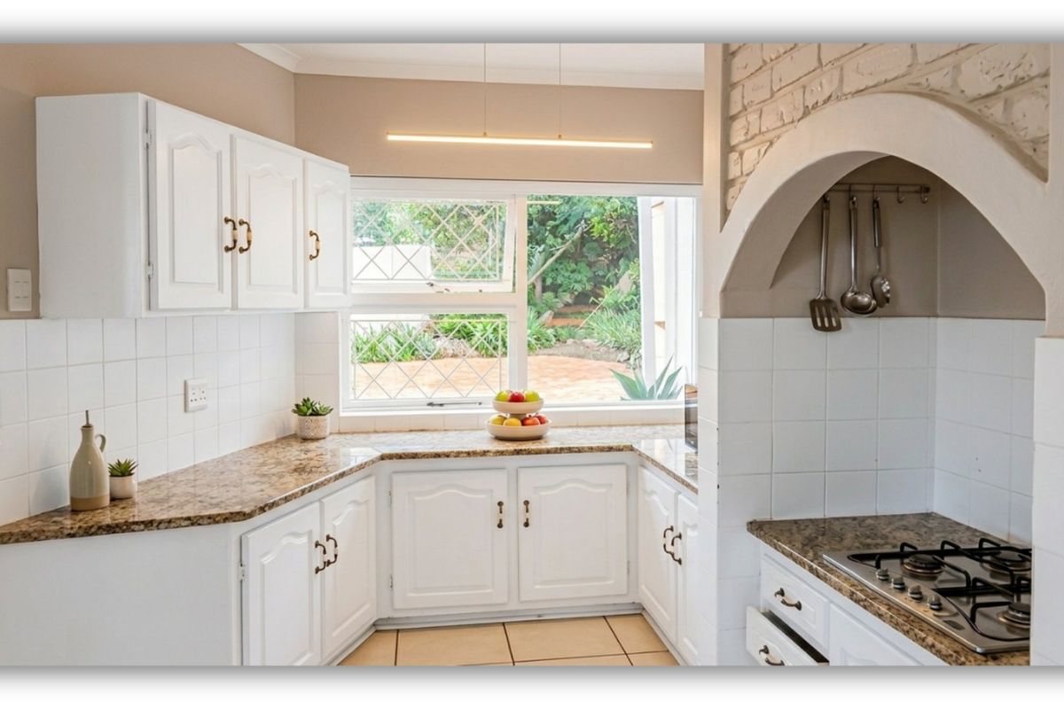 A well-maintained kitchen featuring white cabinetry, granite countertops, a gas hob, and a distinctive brick arch detail overlooking the garden.