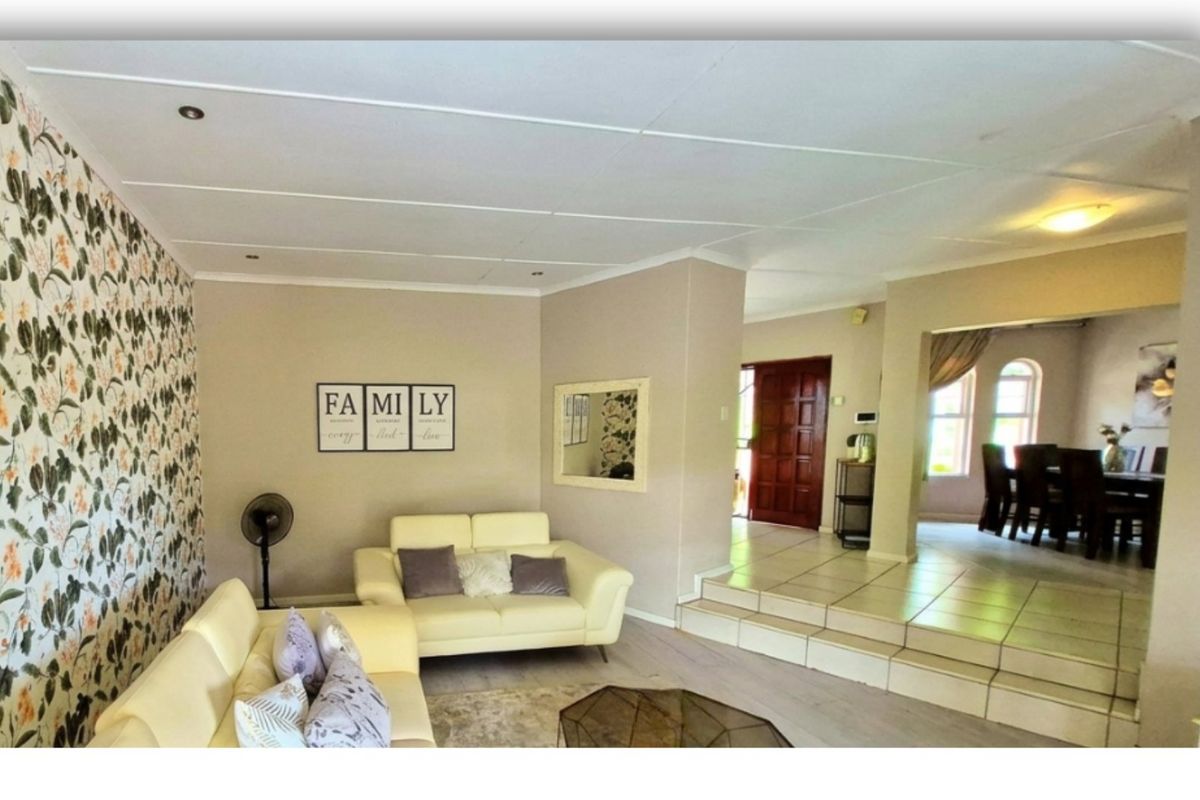 Spacious living area featuring tiled flooring, a raised platform transition to the dining space, and a decorative feature wall.