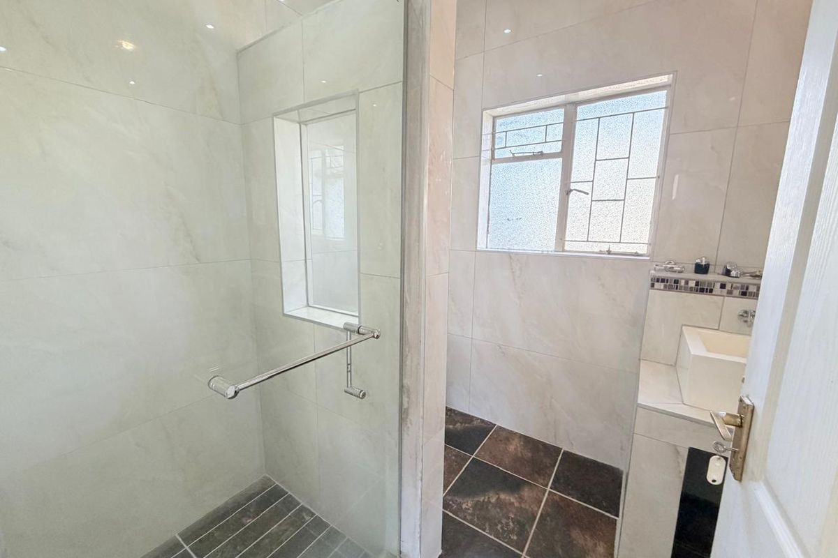 A modern bathroom featuring a glass-enclosed shower, built-in vanity with basin, and neutral wall tiling with contrasting floor tiles.