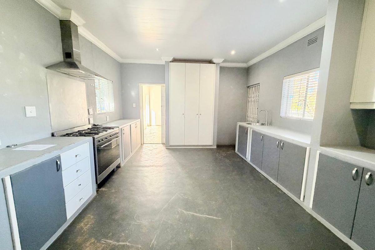 Spacious kitchen featuring grey cabinetry, stainless steel gas stove with extractor, double sink, and ample built-in storage space.