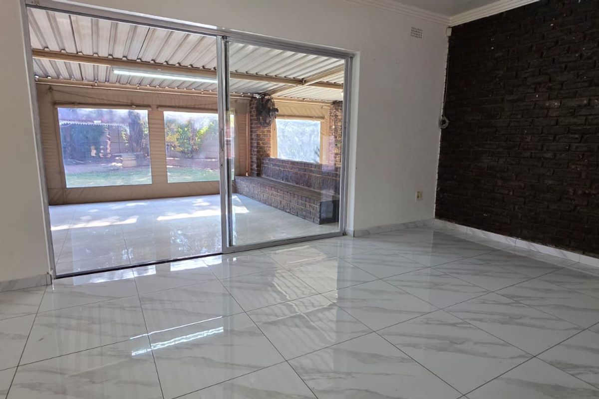 Bright living area featuring modern white marble-look tile flooring, a striking dark exposed brick feature wall, and large sliding doors opening to a covered patio.