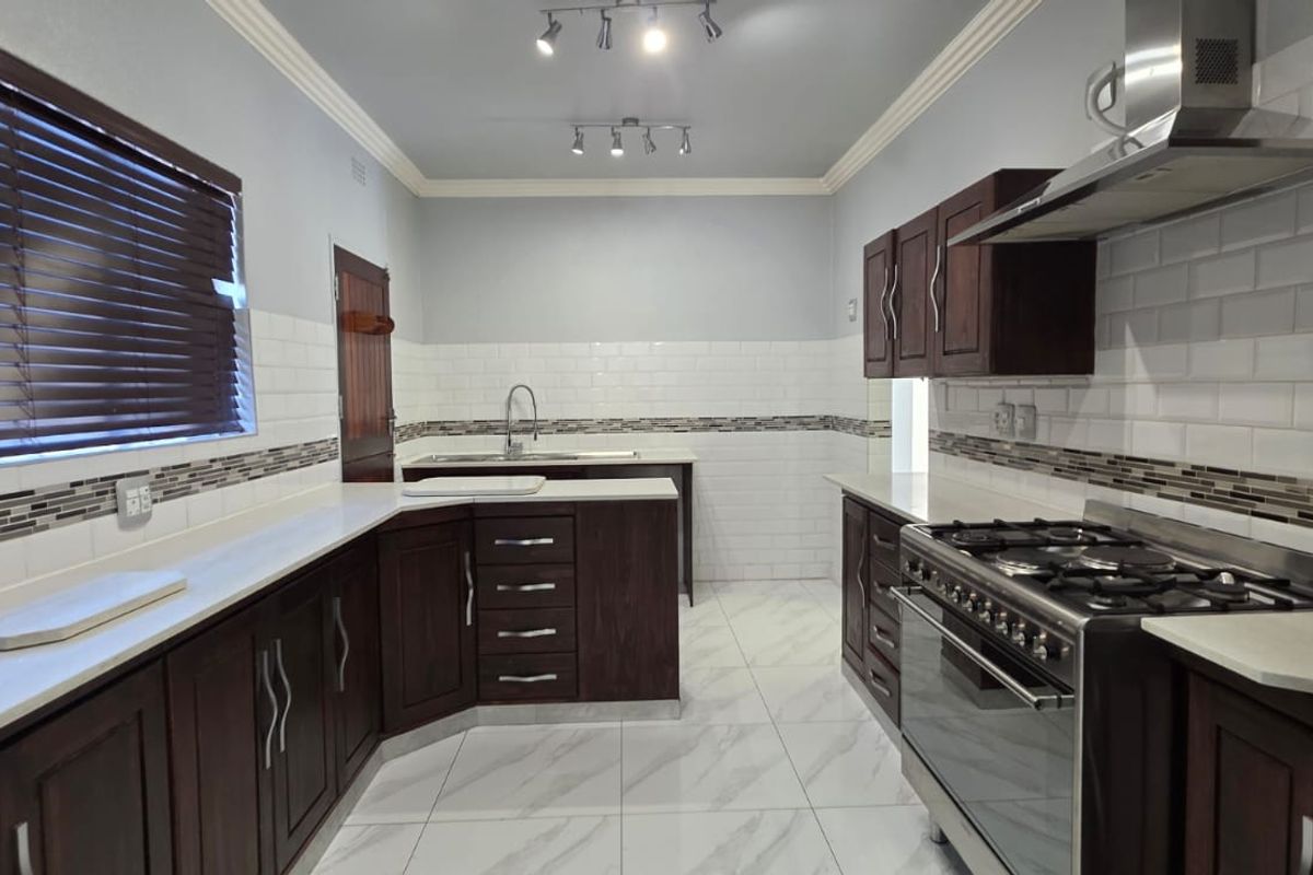 Modern kitchen featuring dark wood cabinetry, white stone countertops, subway tile backsplash, gas stove with extractor fan, and polished porcelain floor tiles.