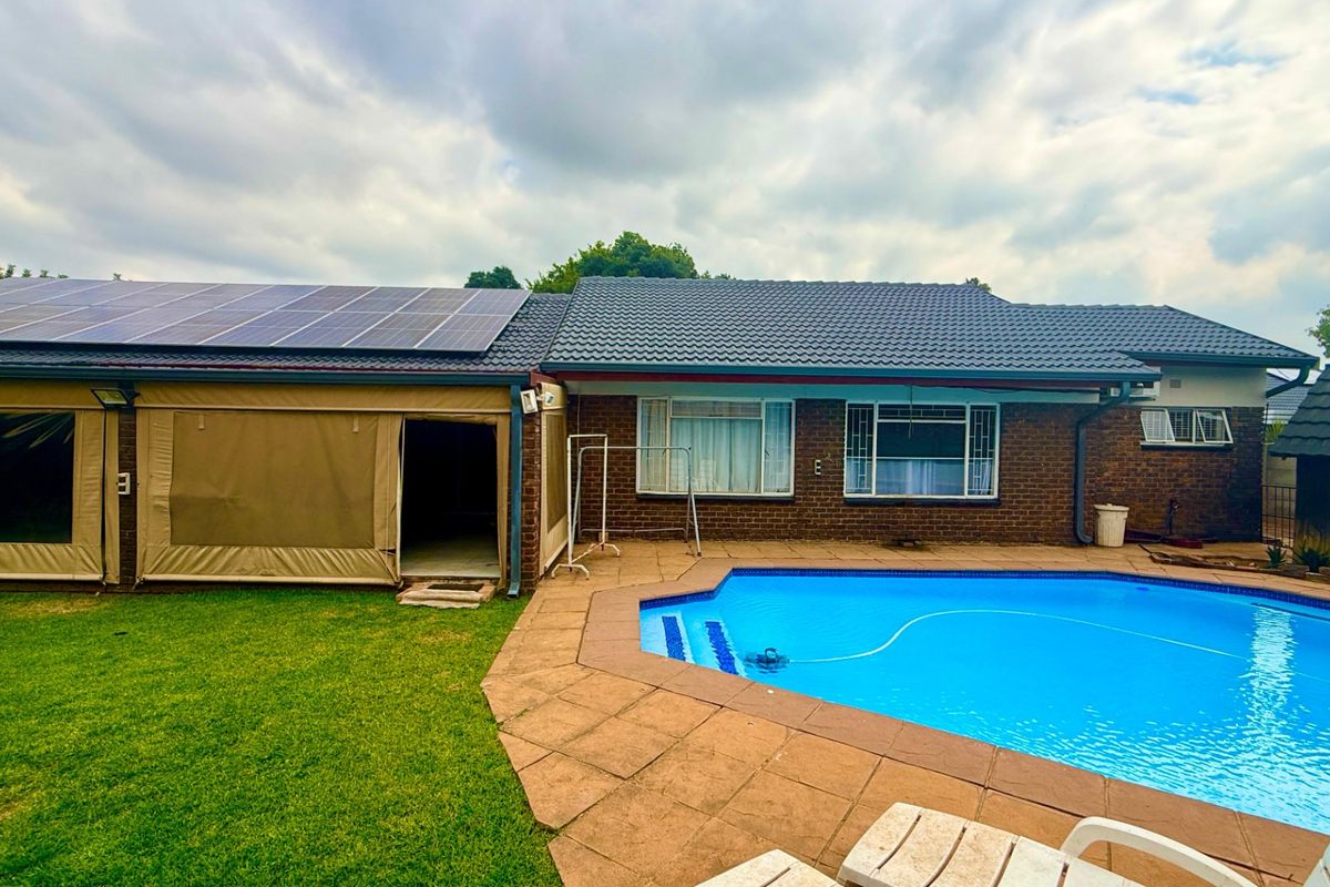 Rear view of the property featuring a swimming pool, paved deck, brick exterior, and a roof equipped with solar panels.
