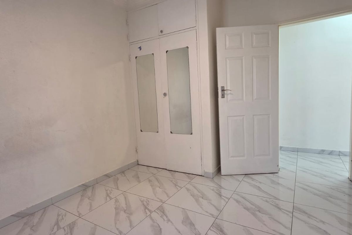 An empty bedroom featuring modern marble-look tiled flooring and built-in cupboards with integrated mirrors, offering a clean canvas for personalization.
