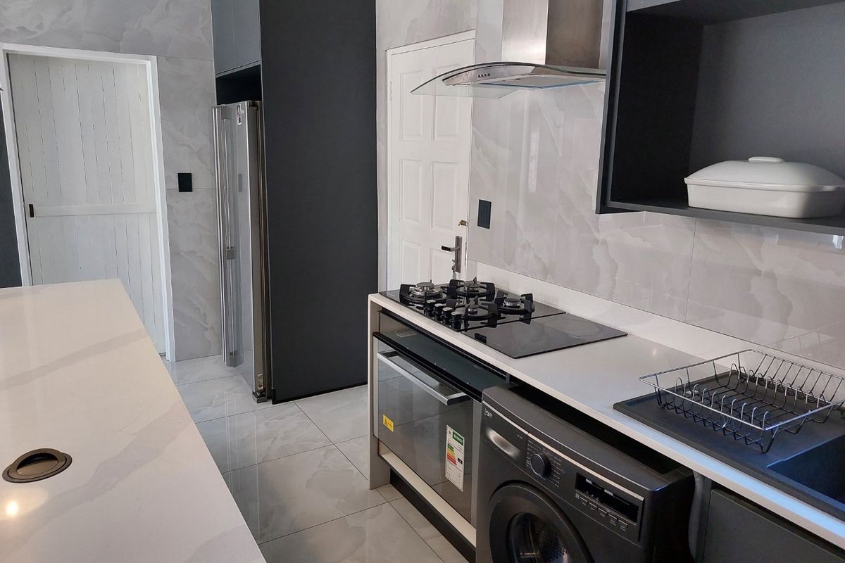 Modern kitchen featuring sleek dark cabinetry, stone countertops, marble-look wall tiles, gas hob, extractor fan, and integrated appliances.