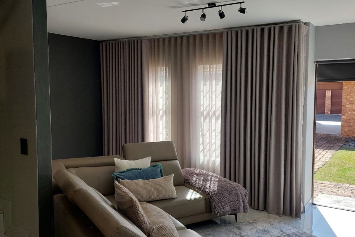 A modern living room featuring tiled flooring, track lighting, and floor-to-ceiling curtains with direct access to an outdoor area.