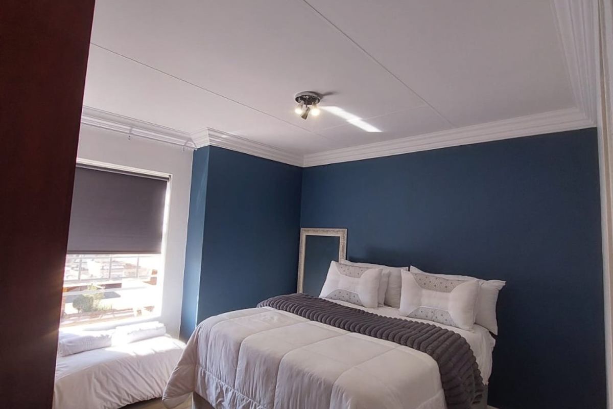 A well-maintained bedroom featuring laminate flooring, crown molding, and a deep blue accent wall with natural light from the window.