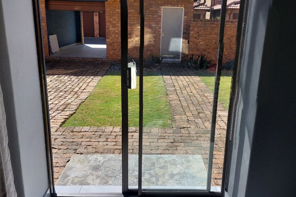 View from an interior space looking out through a sliding glass door onto a brick-paved courtyard and garden area.