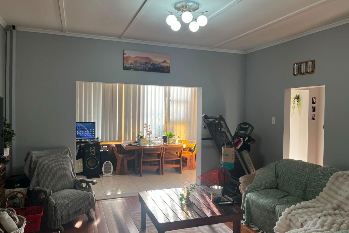 A living room featuring hardwood flooring and a large opening leading to an adjacent dining area with vertical blinds.