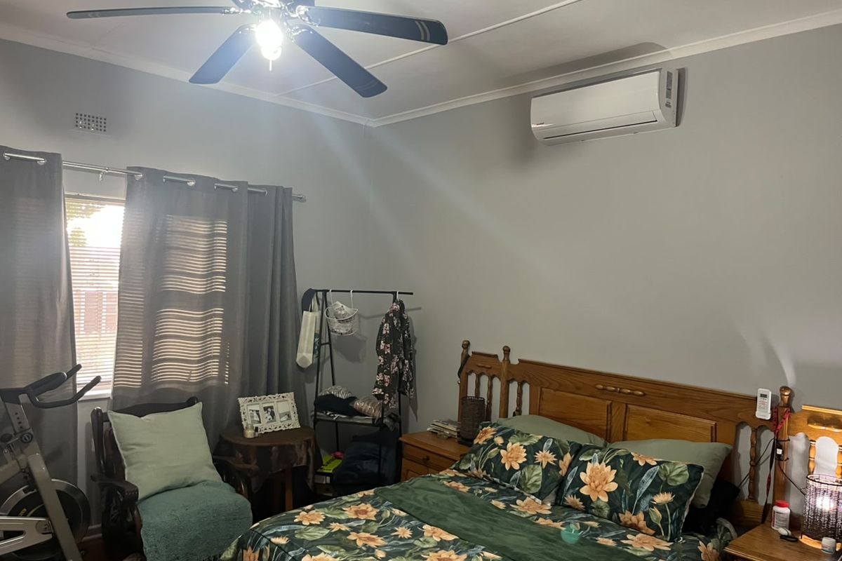 A functional bedroom featuring a ceiling fan and a wall-mounted split-system air conditioning unit for climate control.