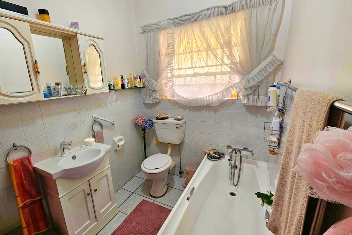 A functional bathroom featuring a vanity cabinet with basin, a wall-mounted mirror cabinet, a standard toilet, and a bathtub with tiled finishes.