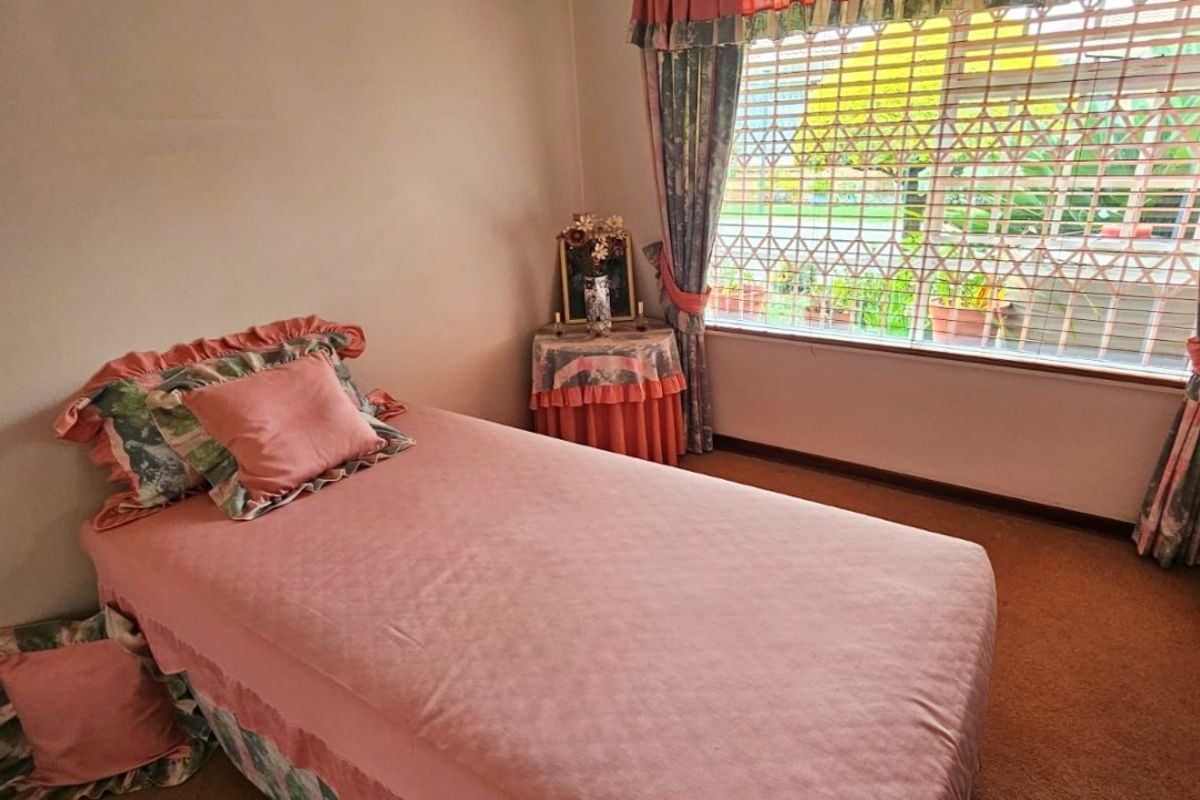 A bedroom featuring carpet flooring and a window fitted with a security gate.