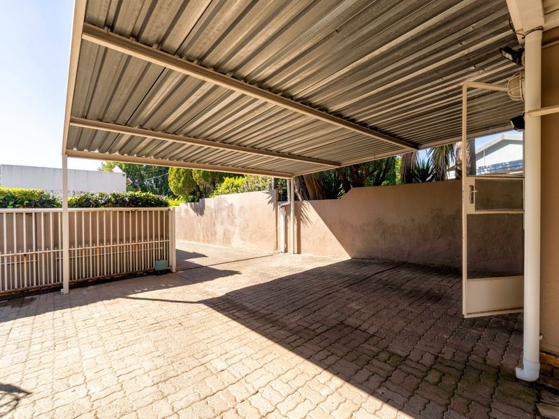 A covered carport area featuring a corrugated metal roof, paved driveway, and secure perimeter walling.