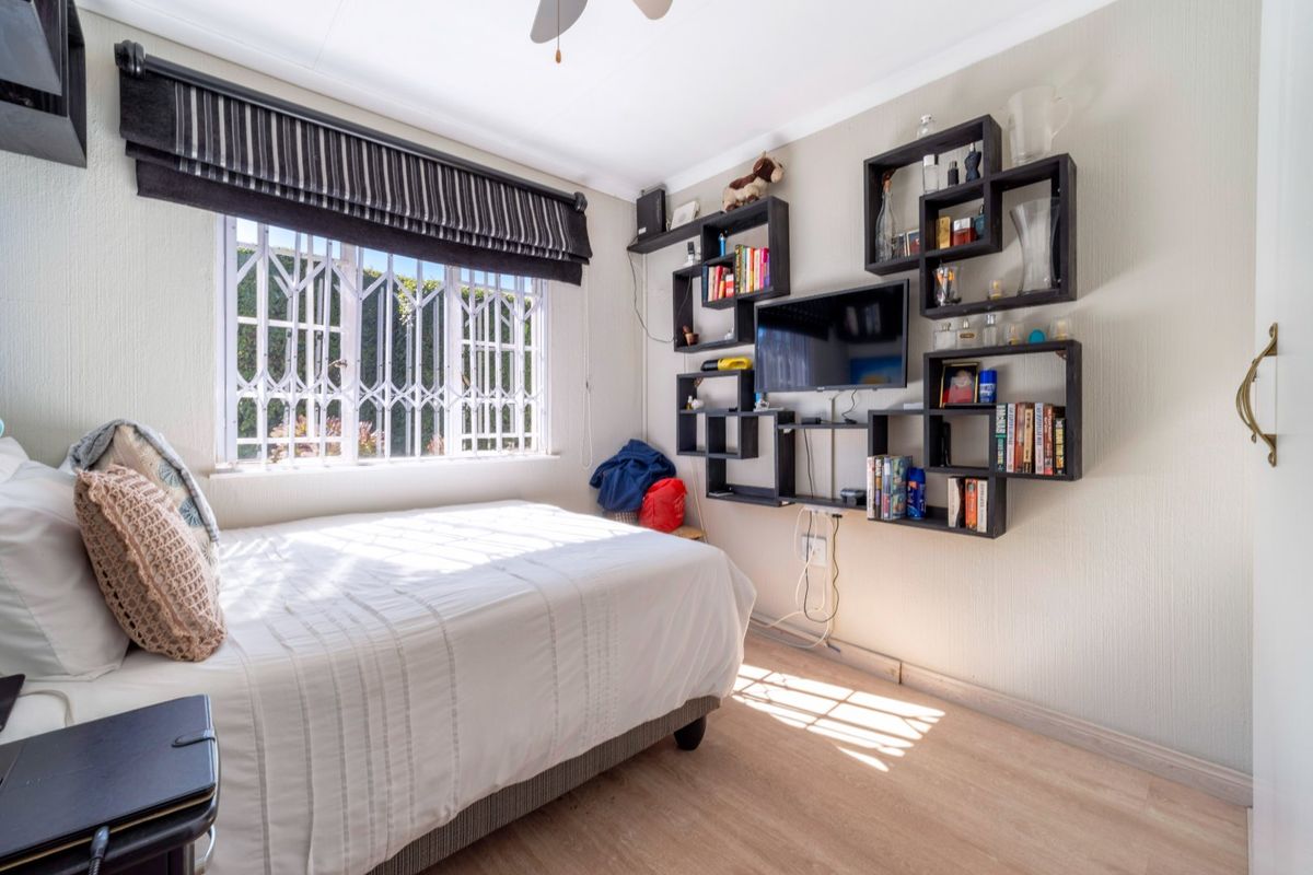 A functional bedroom featuring laminate flooring, a ceiling fan, and built-in wall shelving, with a security gate installed on the window.