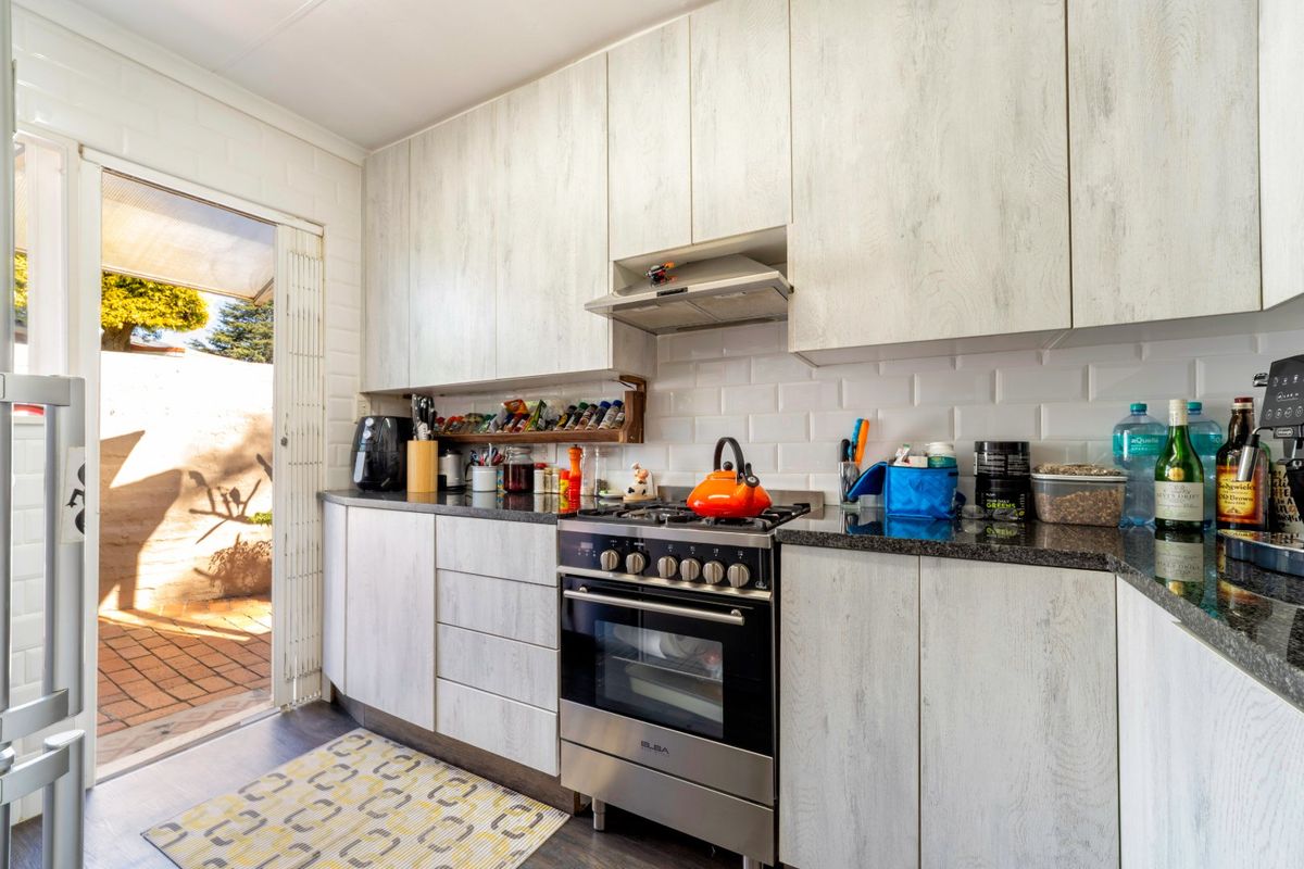 A functional kitchen featuring light wood-grain cabinetry, granite countertops, a subway tile backsplash, and a gas stove, with direct access to an outdoor patio area.