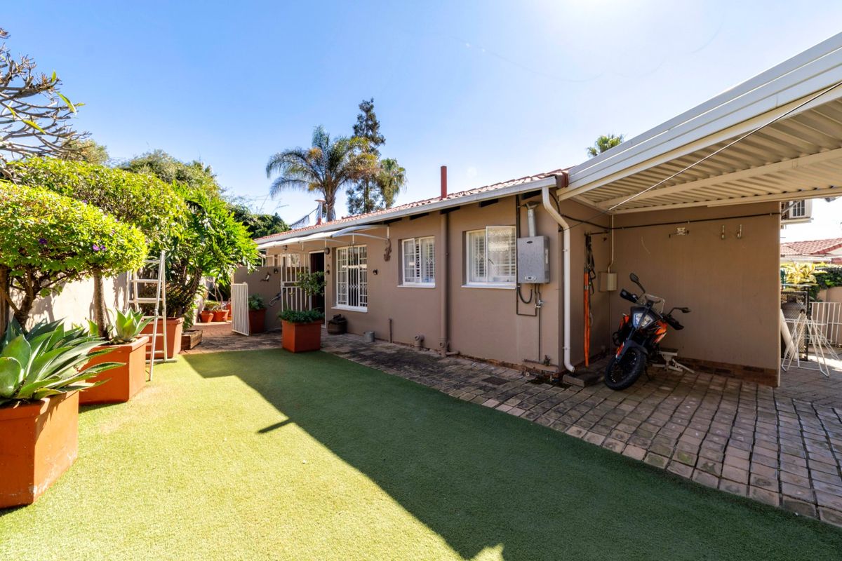 Rear exterior view featuring a paved covered patio area, artificial lawn, and a functional gas geyser installation.