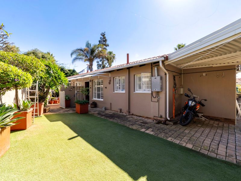 Rear exterior view featuring a paved covered patio area, artificial lawn, and a functional gas geyser installation.
