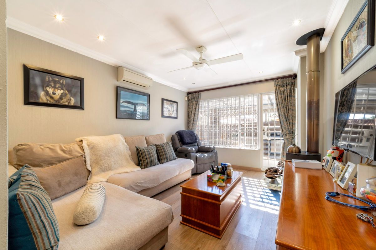 A comfortable living room featuring a wood-burning fireplace, ceiling fan, split-system air conditioning, and laminate flooring with access to an outdoor area.