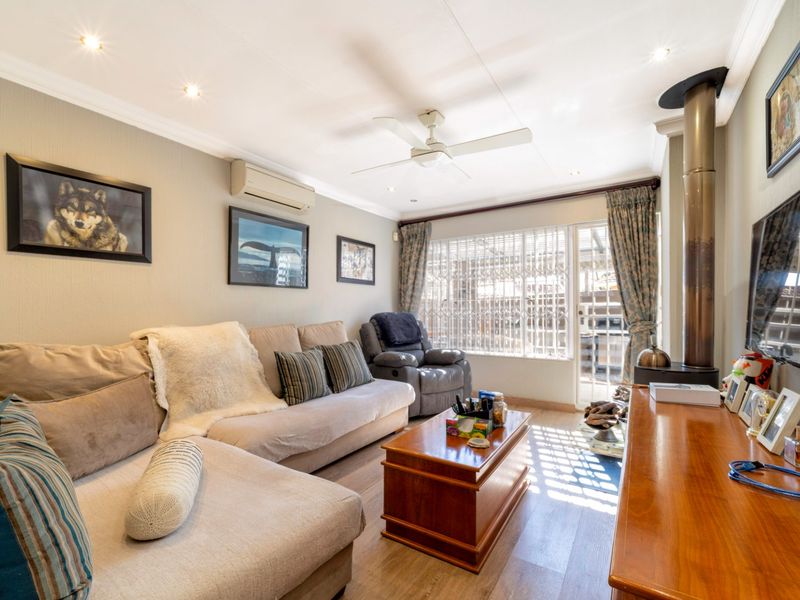 A comfortable living room featuring a wood-burning fireplace, ceiling fan, split-system air conditioning, and laminate flooring with access to an outdoor area.