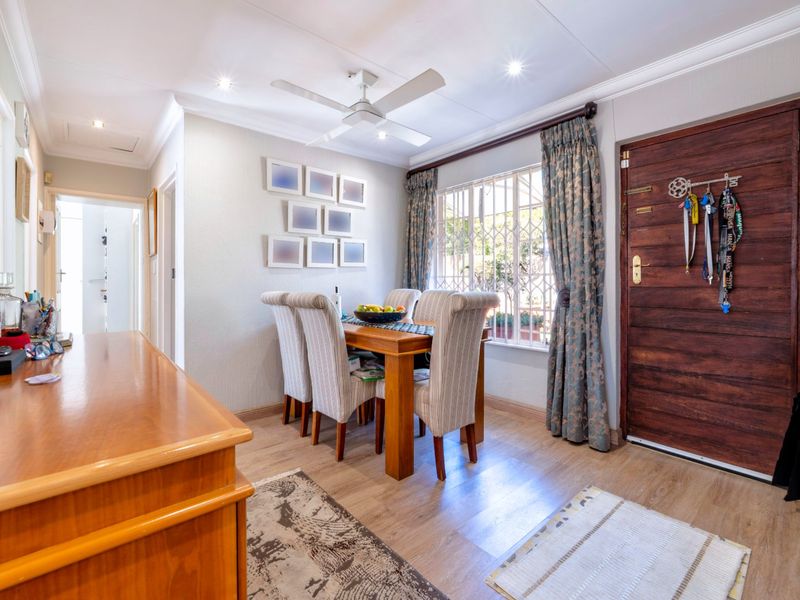 A well-maintained dining area featuring laminate flooring, recessed lighting, a ceiling fan, and a solid timber entrance door with security gate.