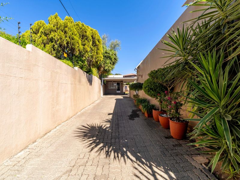 A paved driveway leading to a carport, enclosed by high boundary walls with integrated electric fencing and established garden pots.