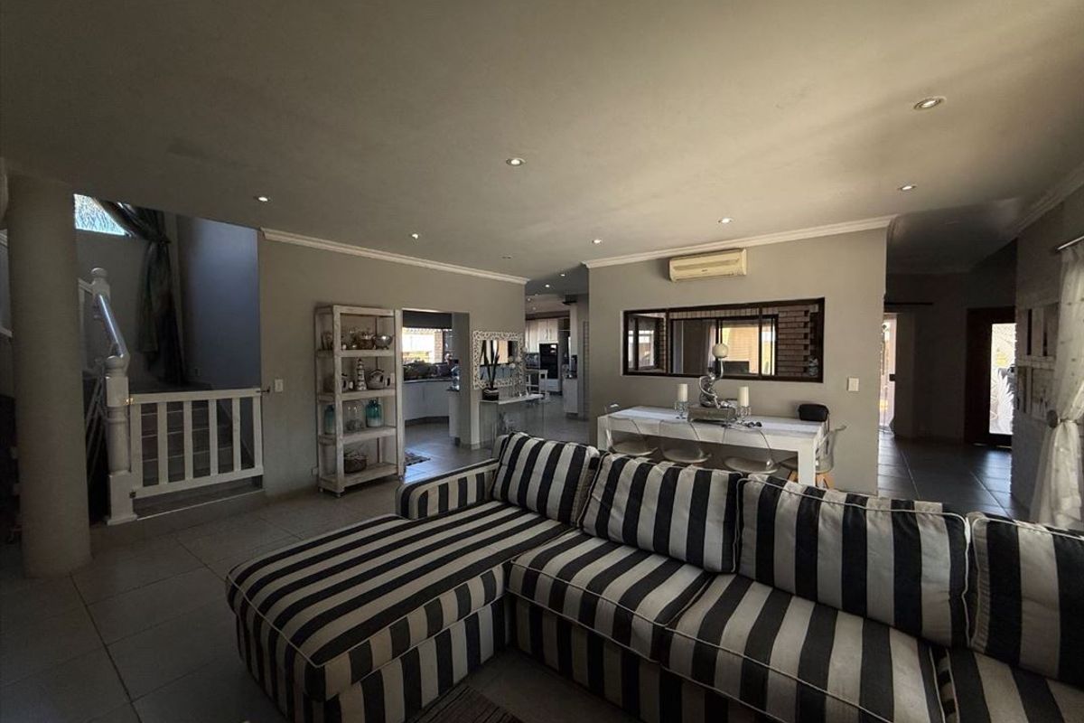 Spacious open-plan living and dining area featuring tiled floors, recessed lighting, and a split-system air conditioner, with an adjoining staircase and kitchen access.