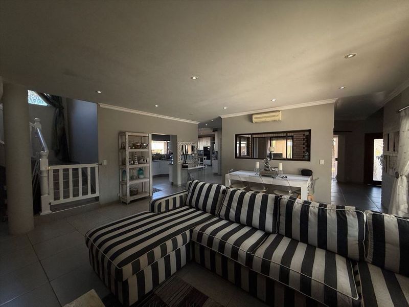 Spacious open-plan living and dining area featuring tiled floors, recessed lighting, and a split-system air conditioner, with an adjoining staircase and kitchen access.