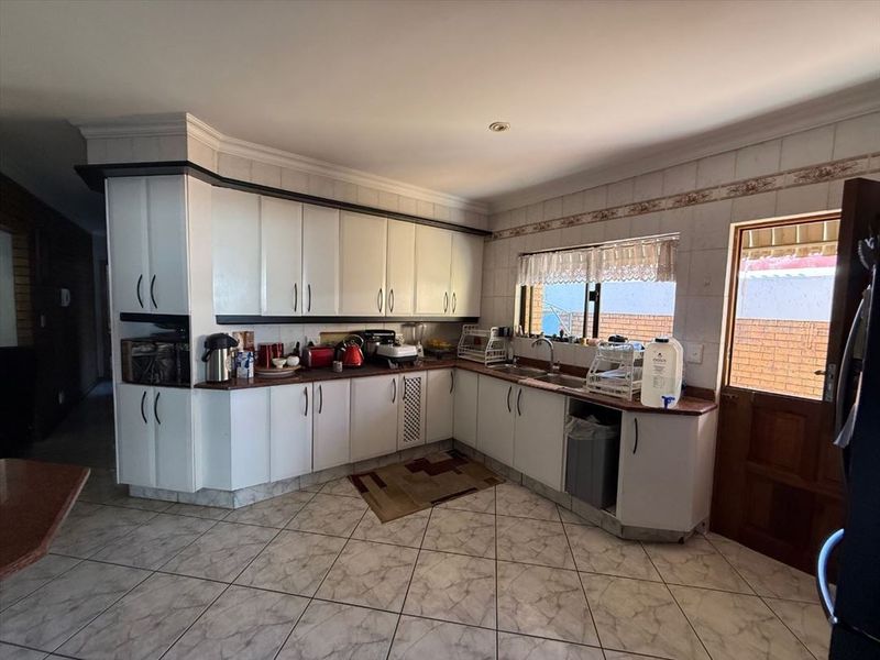 A functional kitchen featuring white cabinetry, laminate countertops, a double basin sink, and tiled flooring with direct access to the exterior.