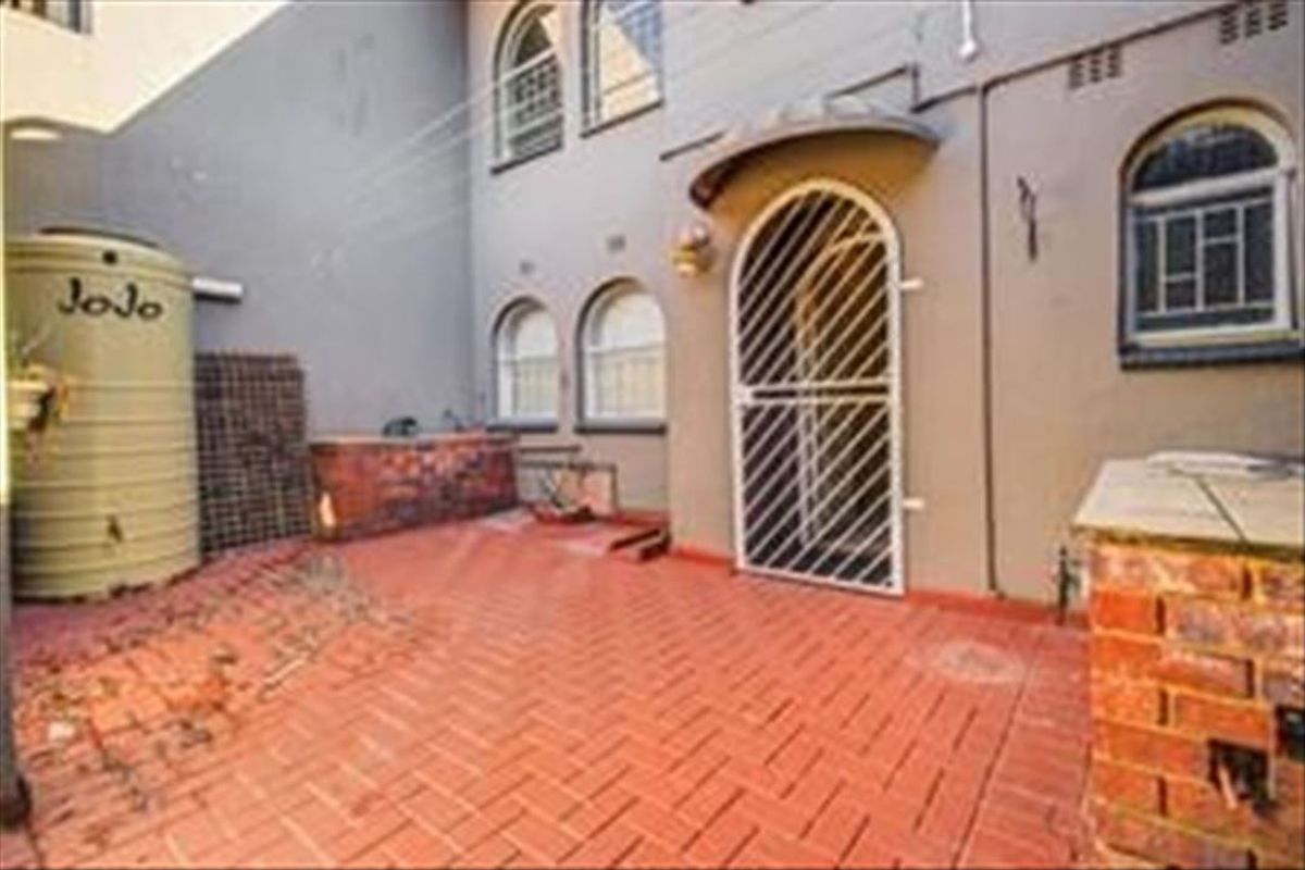 Rear courtyard area featuring brick paving, a water storage tank, and a secure entrance with arched windows.