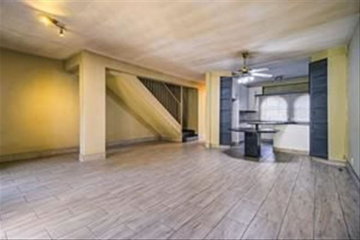Spacious open-plan living area featuring tiled flooring, a central staircase, and an integrated kitchen with breakfast bar, requiring cosmetic updates.
