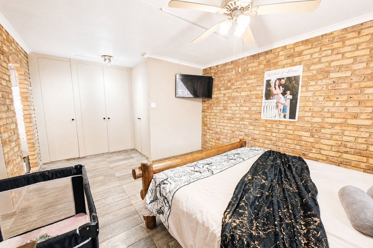 A bedroom featuring an exposed brick feature wall, built-in cupboards, tiled flooring, and a ceiling fan.