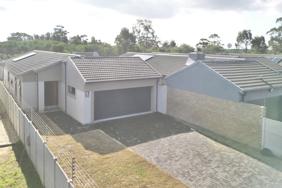 Aerial view of a residential property featuring a tiled roof, paved driveway, garage, and secure perimeter wall with electric fencing.