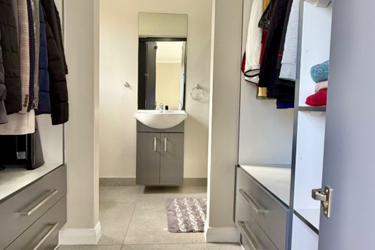 A walk-in dressing area featuring modern built-in cabinetry and tiled flooring, leading directly into a compact en-suite vanity area.