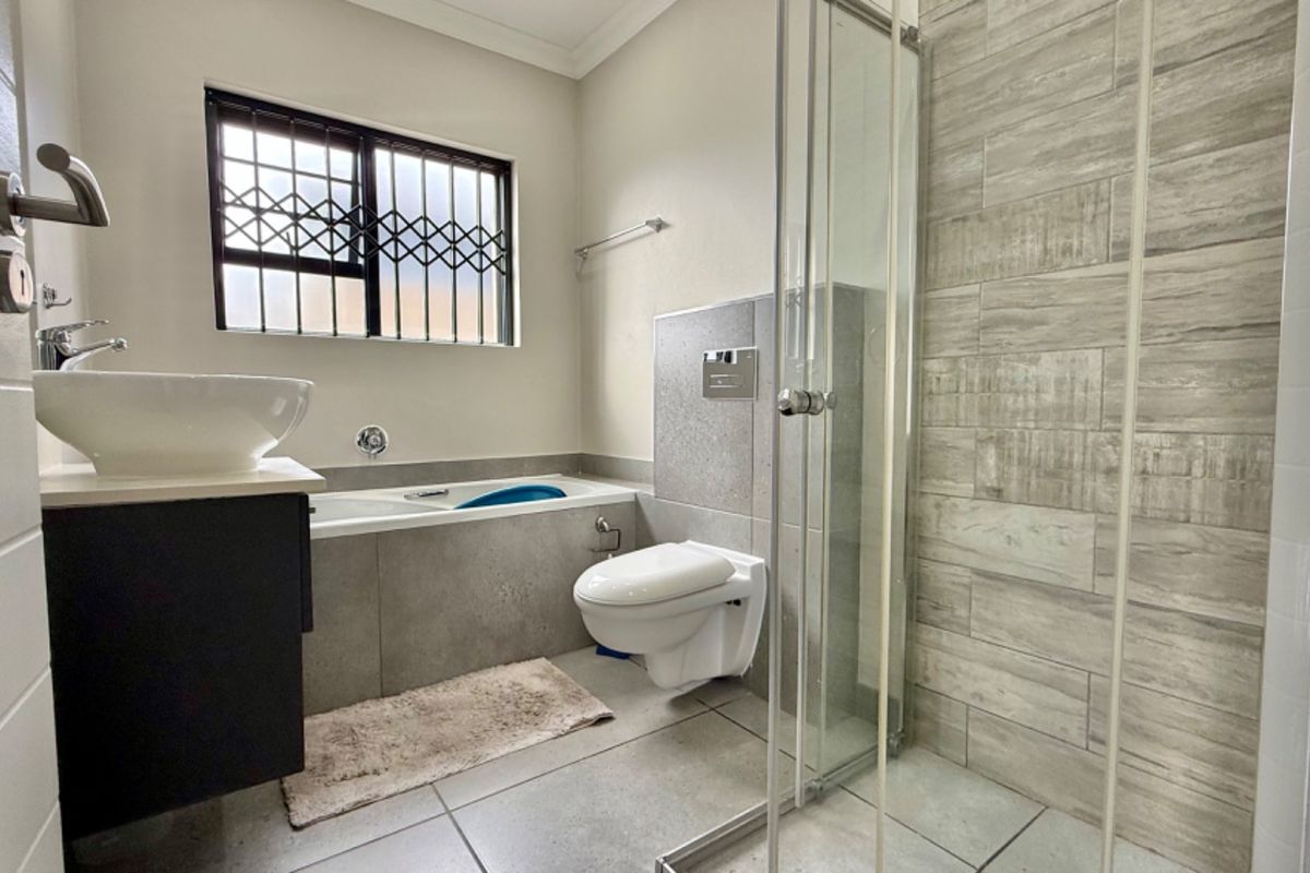 Modern bathroom featuring a vessel sink, built-in bathtub, wall-mounted toilet, and a glass-enclosed shower with textured wall tiling.