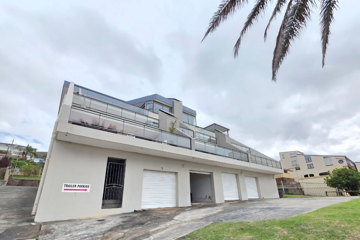 Rear view of a modern apartment complex featuring multiple roller shutter garage doors, glass-fronted balconies, and a paved driveway area.
