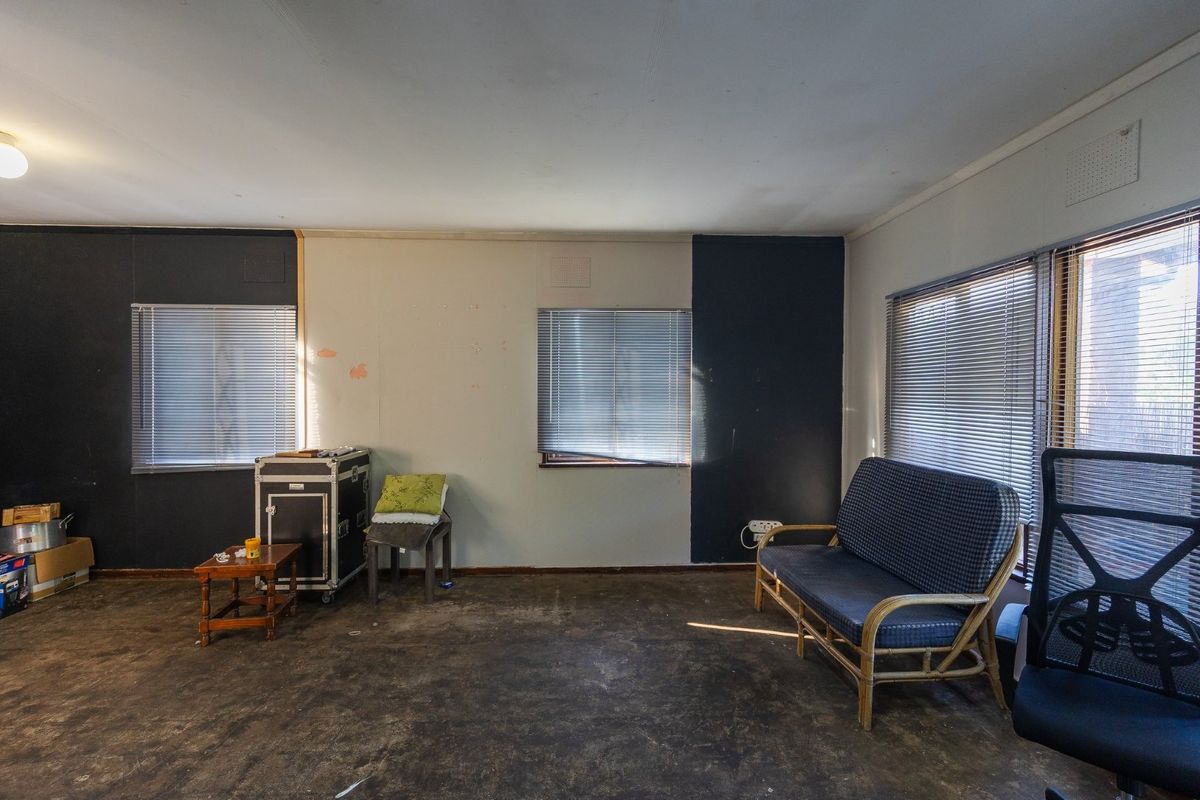 A living room space featuring dark accent walls, venetian blinds, and worn flooring, offering a blank canvas for renovation and interior design updates.