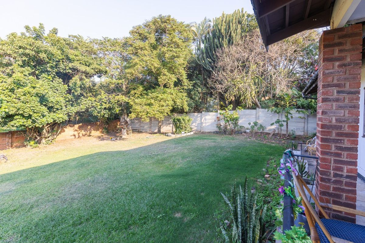 A spacious rear garden featuring a well-maintained lawn, mature trees, and a secure precast concrete boundary wall.