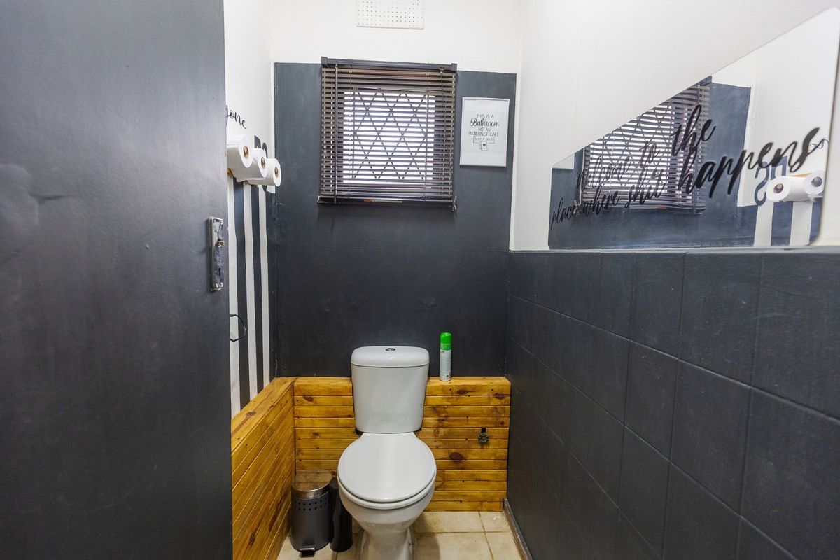 A compact bathroom featuring a toilet, dark wall tiling, and timber wall cladding accents.