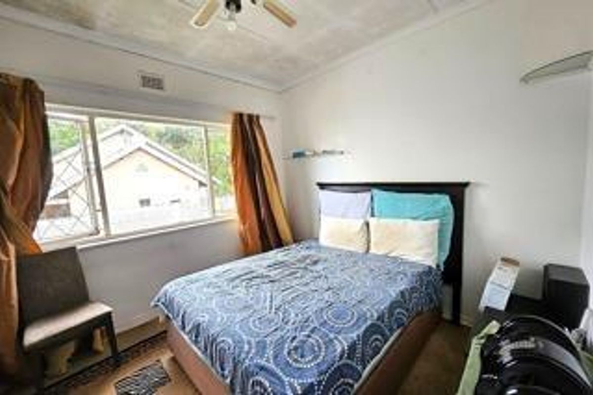 A bedroom featuring a ceiling fan and a large window with security bars, requiring cosmetic updates to improve its overall condition.