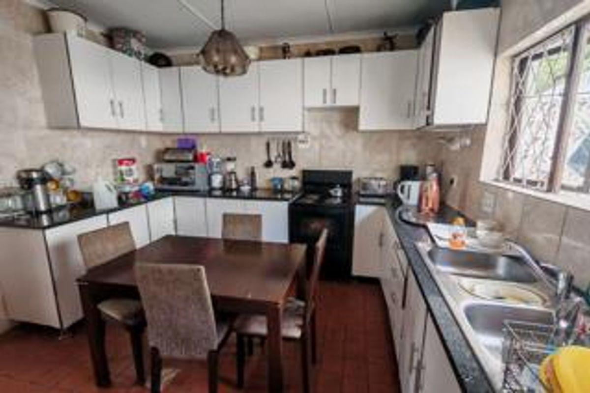 A functional kitchen featuring white built-in cabinetry, a double basin sink, tiled backsplash, and an electric stove with a dining area.