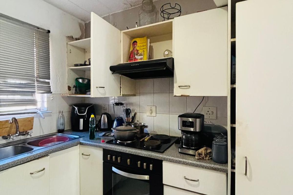 Compact kitchen featuring built-in oven, hob, extractor fan, and double sink with tiled backsplash and flooring, requiring cosmetic updates.