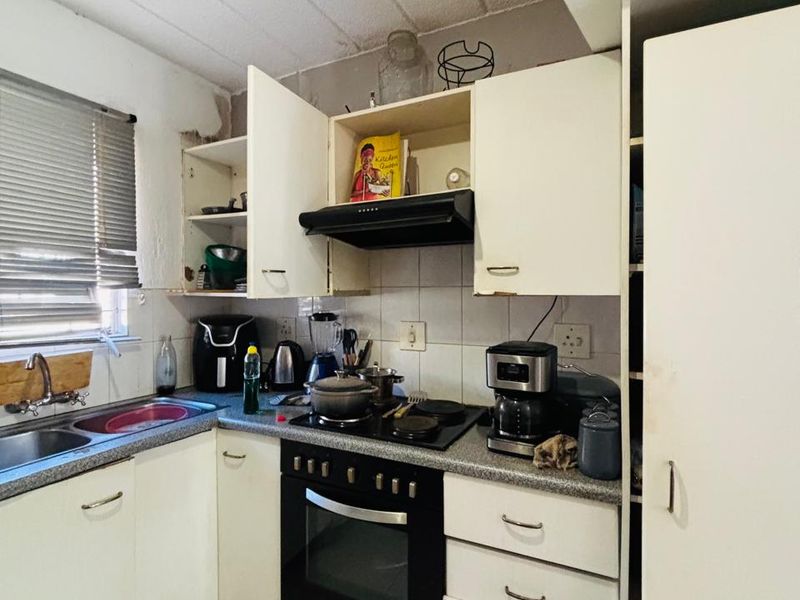 Compact kitchen featuring built-in oven, hob, extractor fan, and double sink with tiled backsplash and flooring, requiring cosmetic updates.