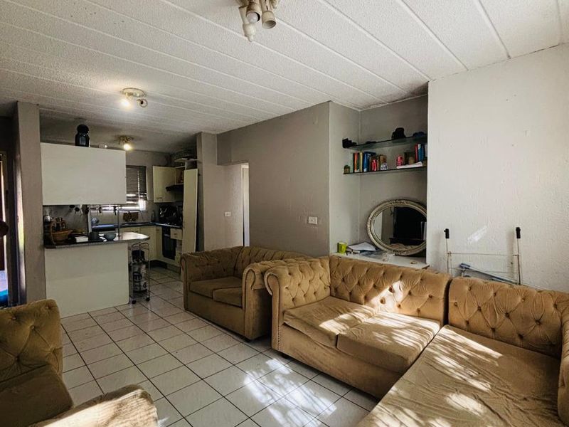 Open-plan living area featuring tiled floors and a connected kitchen space with built-in cabinetry and a breakfast counter.