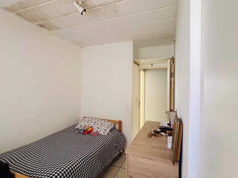 A compact bedroom featuring tiled flooring and a textured ceiling with visible water staining, requiring maintenance and cosmetic updates.