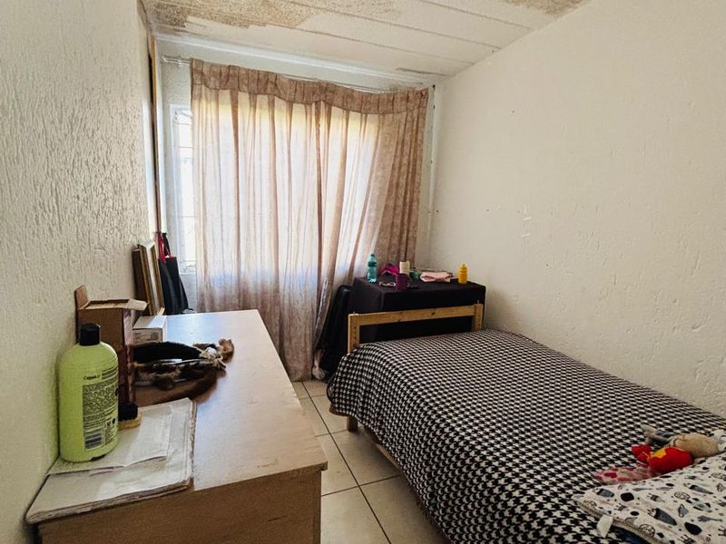 A compact bedroom featuring tiled flooring and a textured ceiling. The space requires maintenance and cosmetic updates to improve its overall condition.