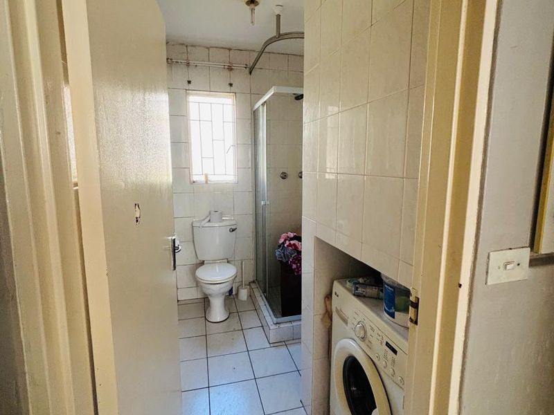 A functional bathroom featuring tiled finishes, a shower enclosure, a toilet, and a dedicated space for a laundry appliance.