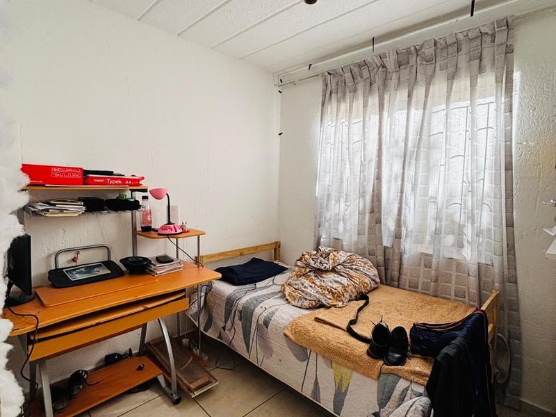 A compact bedroom featuring tiled flooring and a window with a curtain track, requiring cosmetic updates to improve the overall finish.