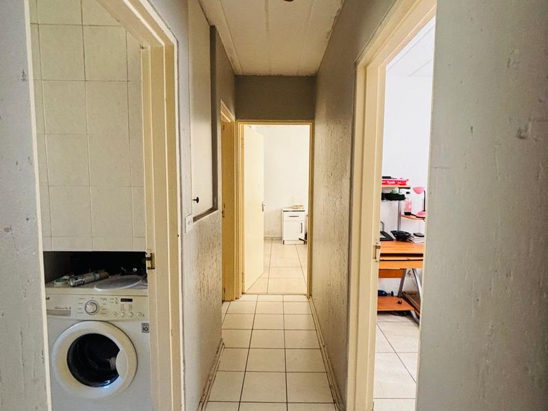 A narrow hallway featuring tiled flooring and a dedicated laundry nook, currently showing significant signs of wear and requiring cosmetic refurbishment.