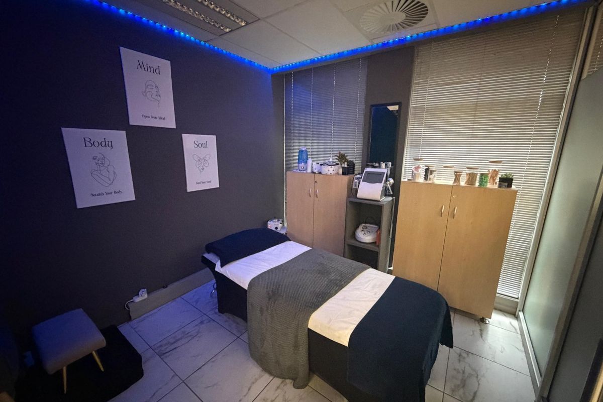 A professional treatment room featuring tiled flooring, built-in storage cabinetry, venetian blinds, and recessed ceiling lighting with ambient blue accent lighting.